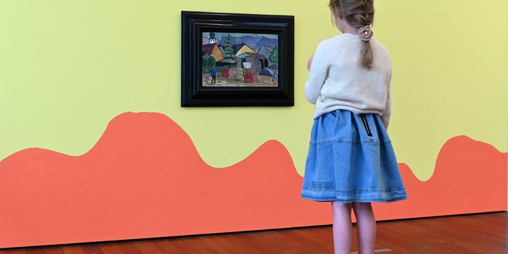 Ein Mädchen betrachtet ein Gemälde von Gabriele Münter. Die Wand ist in Orange und Gelb bemalt.