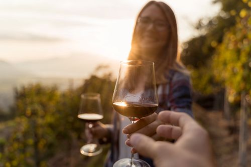 Frau reicht Mann einen Wein im Weinberg bei der Weinprobe