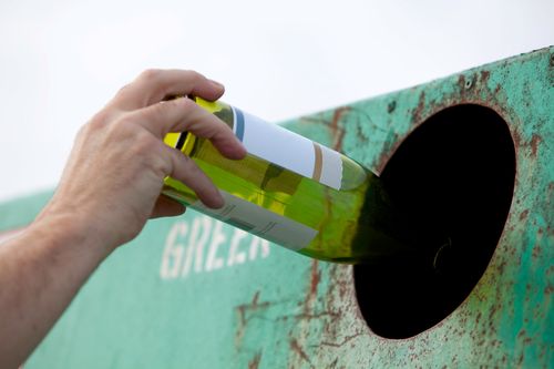 Mann wirft grüne Flasche in Glascontainer