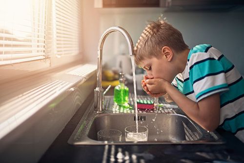 Junge trinkt Wasser aus Küchenwasserhahn
