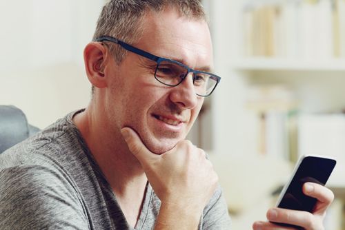 Mann mit Hörhilfe und Brille schaut auf sein Smartphone