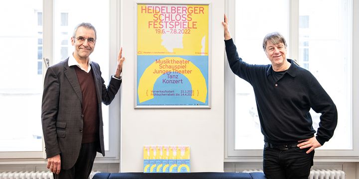 Dramaturg Jürgen Popig und Intendant Holger Schultze stehen neben einem Plakat der Heidelberger Schlossfestspiele 2022