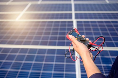 Hand mit Messgerät vor Solarpanels
