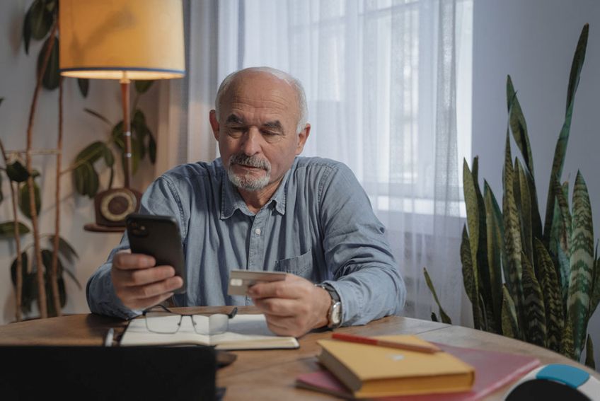 Senior zuhause mit Smartphone und Versicherungskarte