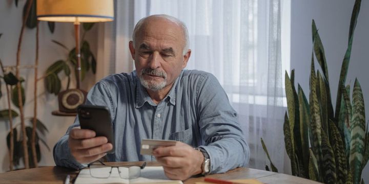 Senior zuhause mit Smartphone und Versicherungskarte