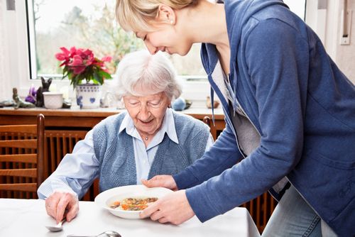 Pflegekraft serviert Seniorin zuhause das Essen