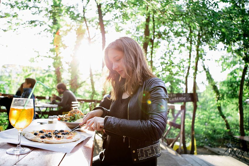 Frau isst Pizza im Außenbereich eines Restaurants unter Bäumen