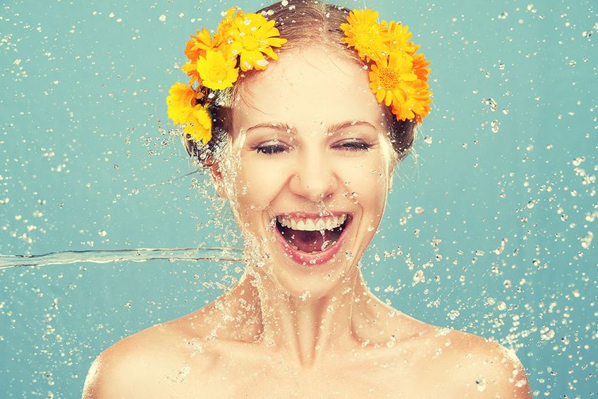 Frau mit Blumen im Haar wird mit Wasser erfrischt