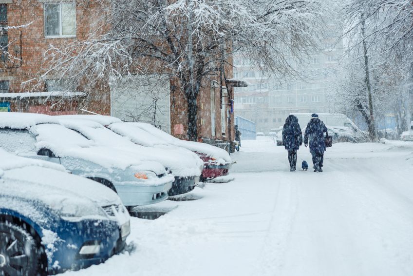 Verschneite Straße mit parkenden Autos und Fußgängern