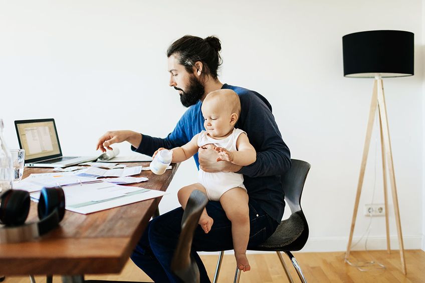 Vater im Home Office mit Baby auf dem Schoß