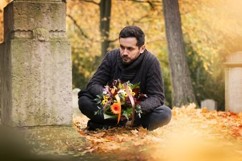 Mann an Allerheiligen auf dem Friedhof mit Blumen