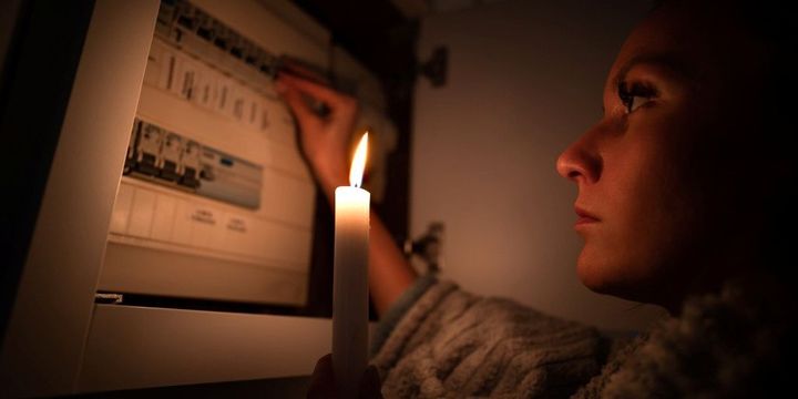 Frau mit Kerze überprüft Sicherungskasten bei Stromausfall