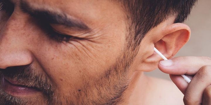 Mann nutzt Wattestäbchen im Ohr und verzieht das Gesicht 