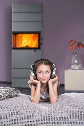 Mädchen hört vor einem Kachelofen Musik mit Kopfhörer