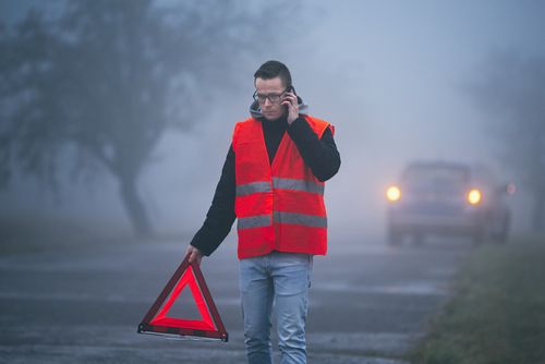 Mann mit Warnweste und Warndreieck setzt Notruf ab nach Unfall im Nebel