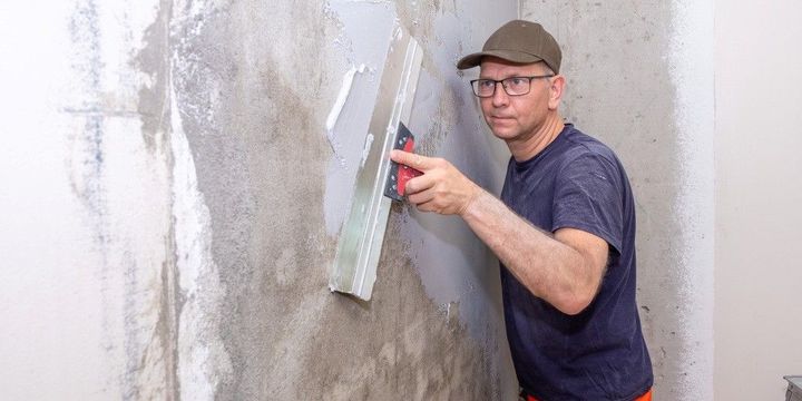 Mann verspachtelt eine Wand und achtet auf Genauigkeit
