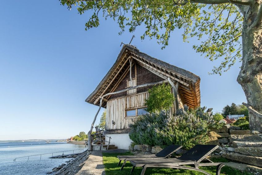 Ein Holzgebäude direkt am Bodensee mit Treppen von der Therme zu einer Liegewiese mit Liegen und zum Bodenseezugang.