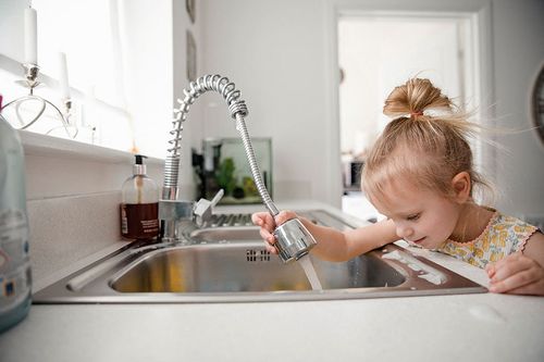 Mädchen betätigt Küchenwasserhahn