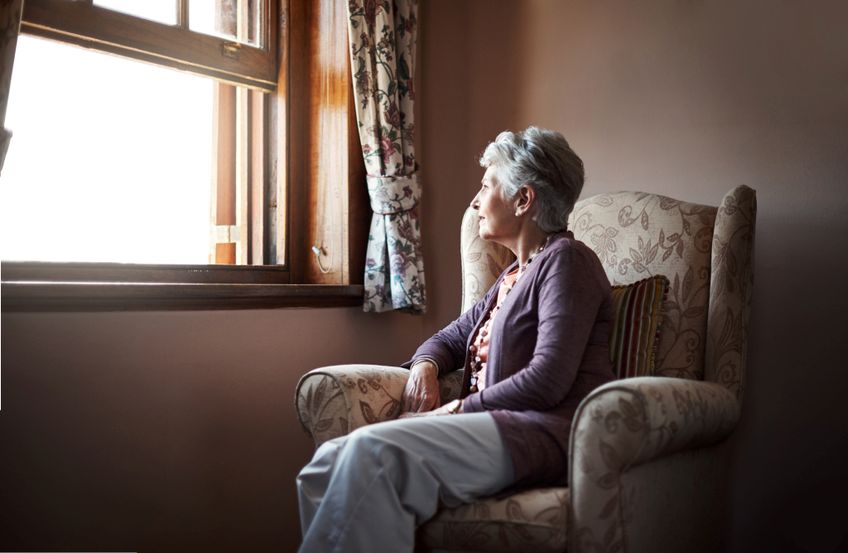 Seniorin im Lehnstuhl schaut traurig aus dem Fenster