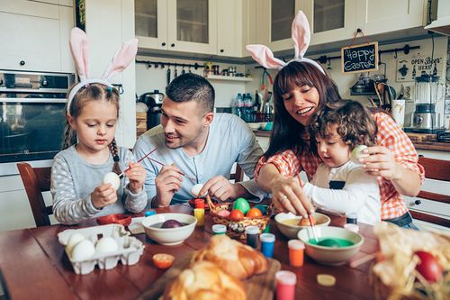 Mutter, Vater und zwei Kindern färben Eier zu Ostern