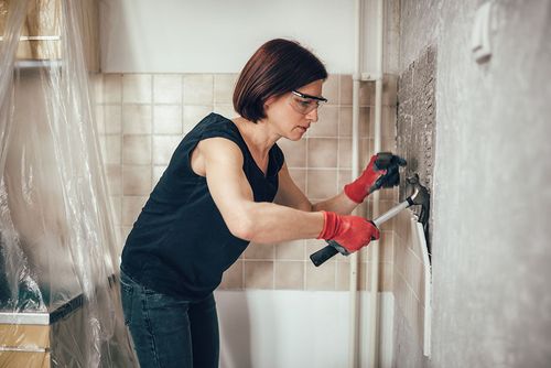 Frau klopft Badezimmerfliesen von der Wand
