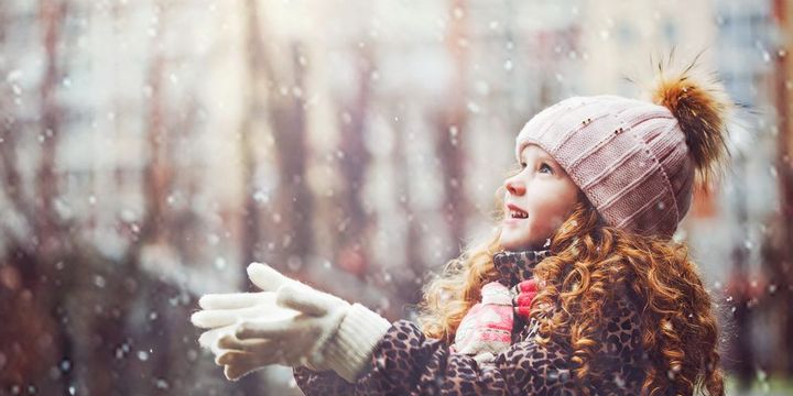 Mädchen mit offenen Händen zum Himmel freut sich über Schnee