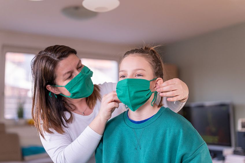 Mutter legt Tochter Mund-Nase-Maske an