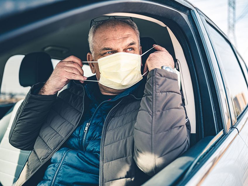 Mann setzt Mund-Nasen-Schutz auf, bevor er aus dem Auto steigt
