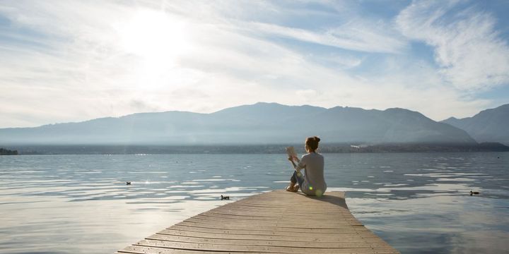 Frau sitz lesend am See auf einem Steg