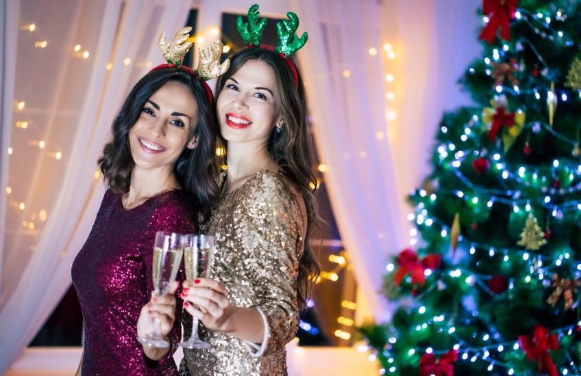 Zwei Frauen mit Glitzeroutfit und Sekt vor Weihnachtsbaum