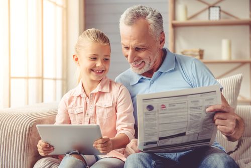 Enkelin und Opa lesen mit Tablet und Zeitung