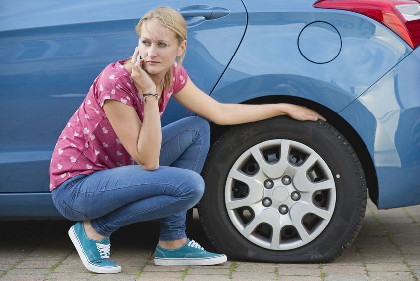 Frau kniet vor Auto mit Reifenpanne