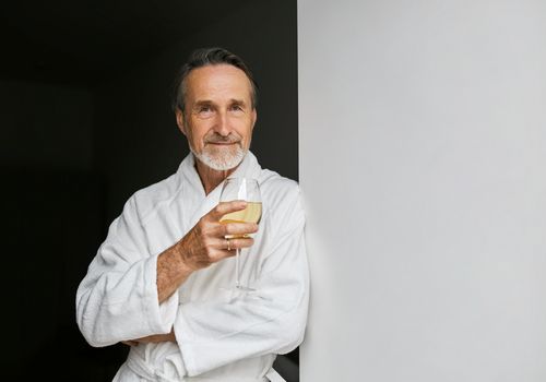 Mann im Wellness-Bademantel hält ein Glas Weißwein