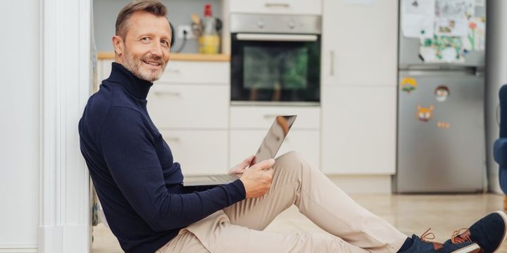 Best Ager sitzt mit Tablet auf Küchenboden