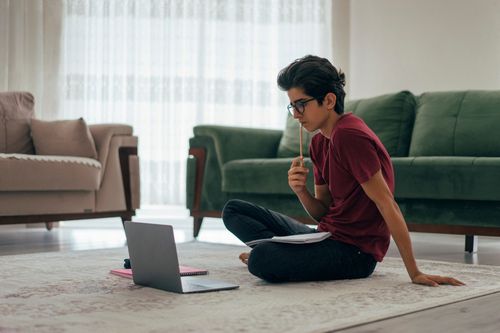 Junger Mann auf dem Boden vor dem Laptop überlegt