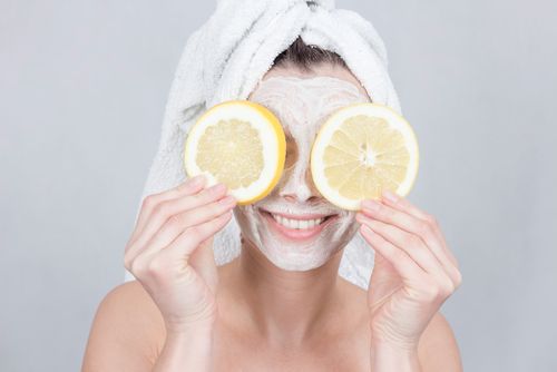 Frau mit Pflegemaske hält Zitronenscheiben vor Augen