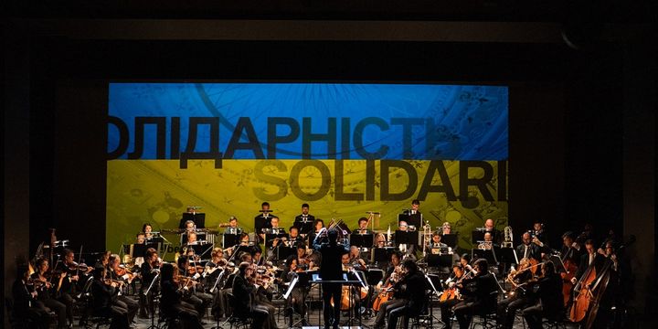 Dirigent und Orchester vor einer blau-gelben Einblendung mit der Aufschrift Солідарність – Solidarität