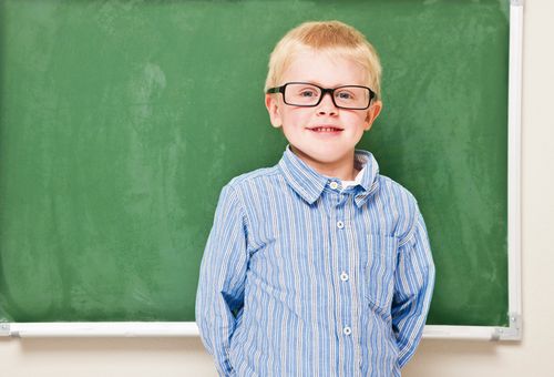 Junge mit Brille vor einer Tafel im Klassenzimmer