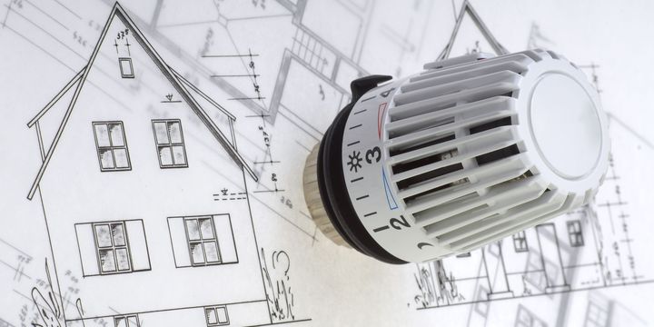 Hier ist ein weißer Thermostatknauf liegend auf gezeichneten Grundrissen und Ansichten von Wohngebäuden zu sehen.