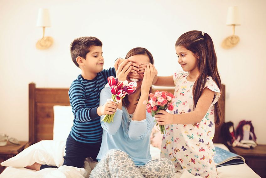 Kinder überraschen ihre Mutter morgens im Bett mit Blumen