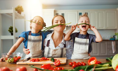 Mutter und zwei Kinder spielen beim Kochen in der Küche mit Spargel